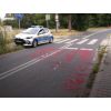 Widok jezdni z namalowanym napisem (zamazanym), w głębi pojazd Straży Miejskiej