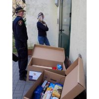 Zdjęcie przedstawiające strażnika miejskiego i wolontariuszkę przy drzwiach wejściowych do  bloku z paczkami żywnościowymi w czasie epidemii