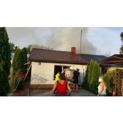 zdjęcie przedstawia płonący dach budynku, służby mundurowe i mieszkańców